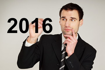 Happy new 2016 year. Handsome thinking businessman writes with marker numeral 2016.