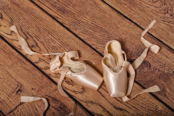 Ballet pointe shoes lie on wooden floor.