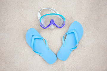 Fototapeta na wymiar beach concept - blue slippers and diving mask on the sand