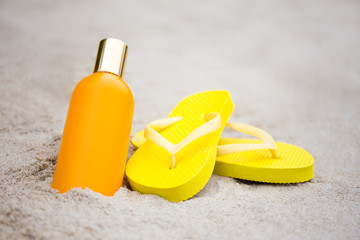 summer concept - slippers and suntan lotion bottle on sandy beac