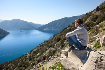 A young man sitting over the sea at the rock and contemplating beautiful Kotor bay in Montenegro