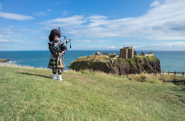 Traditional scottish bagpiper in full dress code at Dunnottar Castle in Stonehaven