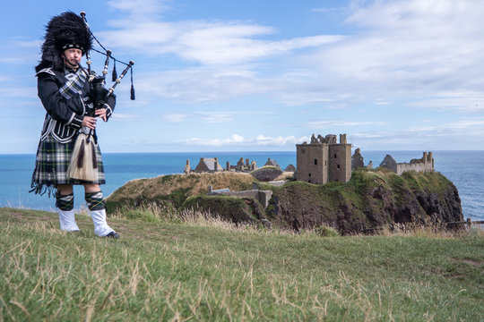 Traditional scottish bagpiper in full dress code at Dunnottar Castle in Stonehaven