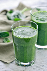 Glasses of spinach juice with napkin on wooden table, closeup