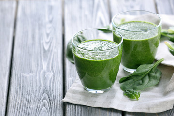 Glasses of spinach juice with napkin on wooden background