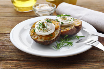 Baked potato mayonnaise and herbs in white plate on wooden table, closeup