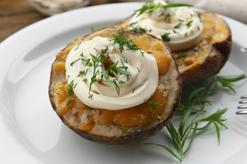 Baked potato with mayonnaise and herbs in white plate, closeup