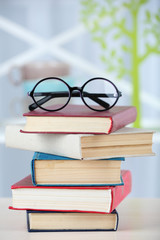 Stack of books with glasses on wooden table in room