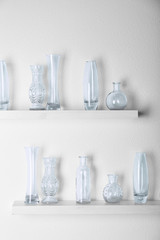 Decorative glass vases on wooden shelf  on white wallpaper background