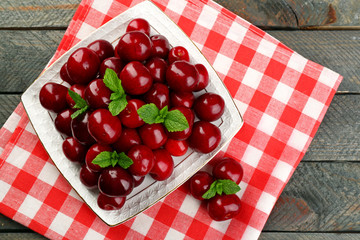 Sweet cherries with green leaves on plate, on wooden background