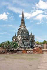 Fototapeta premium Ancient Buddhist temple in Ayutthaya. Thailand. Blackened by time stands among the ruins of the temple against the blue sky with clouds. Bright sunny day.
