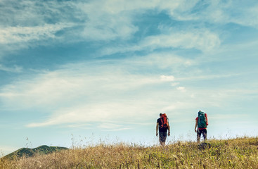 Two mountain travelers with backpacks under blue sky