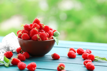 Fresh raspberries in bowl on wooden table on blurred nature background