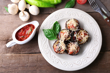 Dish of eggplant with cherry tomatoes and cheese in white plate on wooden table, top view