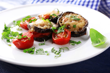 Dish of eggplant with cherry tomatoes and cheese in white plate on wooden table, closeup