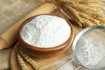 Fototapeta na wymiar Whole flour in bowl with wheat ears on wooden table, closeup
