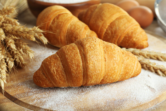 Fresh croissants with flour on wooden table, closeup