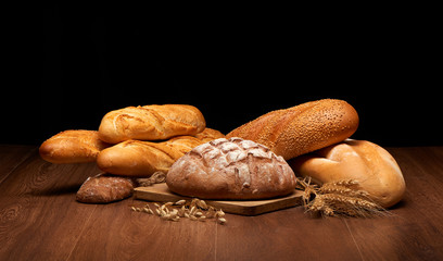 Different bread and wheat on dark wooden table background