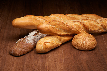 Different baguette breads and bun on dark wooden table background