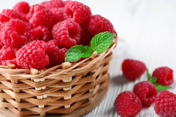 Fresh red raspberries in wicker basket on wooden table, closeup