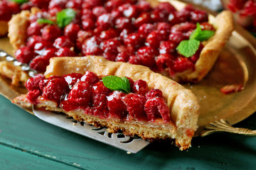 Piece of tart with raspberries on tray, close-up, on color wooden background