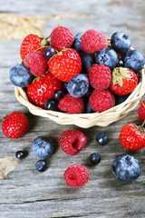 Sweet tasty berries in basket on wooden table close up