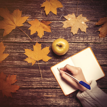 Female hand writing something in notebook next to apple