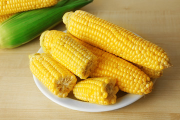 Fresh corn on cobs in plate on wooden table, closeup