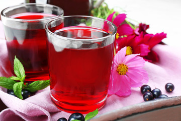 Glasses of fresh blackcurrant juice on wooden tray with pink napkin and flowers, closeup