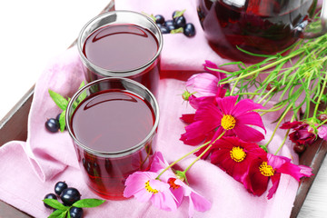 Obraz na płótnie Canvas Glasses of fresh blackcurrant juice on wooden tray with pink napkin and flowers, closeup