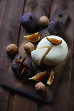 Sliced cheese with figs and walnuts on a rustic cutting board