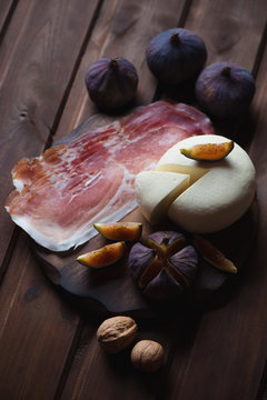 Cheese with ham, figs and walnuts. Dark rustic wooden surface
