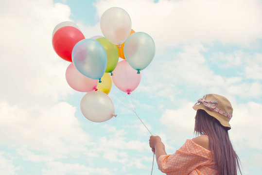 Vintage pastel color of Happy young red hair woman holding colorful balloons and flying on clouds sky background.