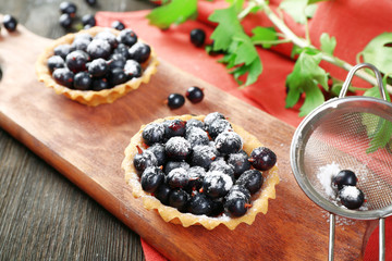 Delicious crispy tarts with black currants on wooden cutting board, closeup