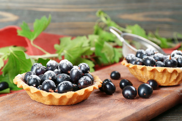 Delicious crispy tarts with black currants on wooden cutting board, closeup