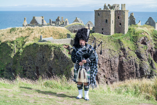 Traditional scottish bagpiper in full dress code at Dunnottar Castle in Stonehaven