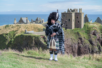 Traditional scottish bagpiper in full dress code at Dunnottar Castle in Stonehaven