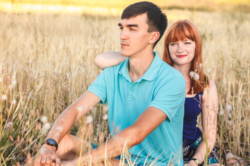 young couple sitting side by side in the field, outdoors