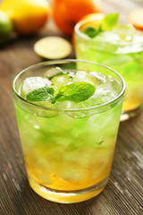 Glasses of lime juice with orange on wooden table, closeup