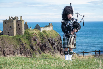 Traditional scottish bagpiper in full dress code at Dunnottar Castle in Stonehaven