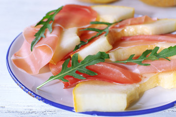 Melon with prosciutto of Parma ham on wooden table, closeup