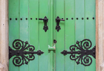 Ancient green door with decorative handle and hinge forged in steel