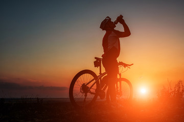 Fototapeta na wymiar Silhouette of a biker and bicycle on sky background.