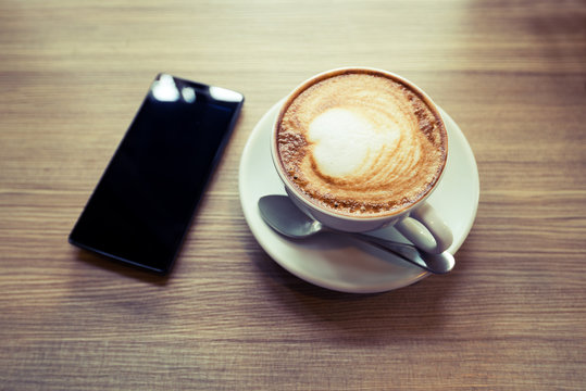 Above view of smart phone with hot cup of coffee on wood table. Photo in vintage color image style.