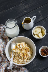 oatmeal with banana, caramel sauce and pecan nuts in a white bowl on a dark wooden surface, a delicious and healthy Breakfast