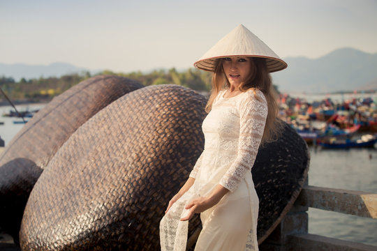 blonde girl in Vietnamese dress touches hat by barrier