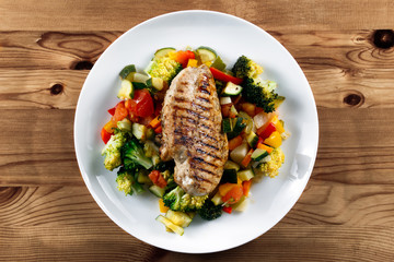 Grilled chicken fillet, breast with cooked vegetable Tomatoes, Carrots, Peppers, Courgettes, brocoli on plates.