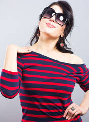 Beautiful brunette in a blue dress with red stripes. Fashion. Portrait of a young girl in sunglasses.
