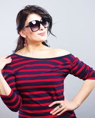 Naklejka premium Beautiful brunette in a blue dress with red stripes. Fashion. Portrait of a young girl in sunglasses. 