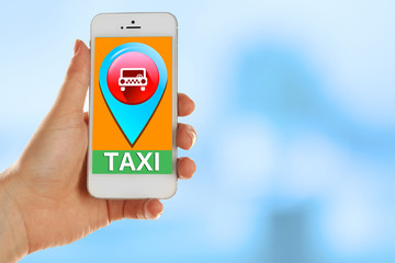 Hands holding mobile smart phone with interface taxi on blue background